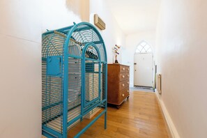 A hallway with a blue birdcage, wooden dresser, and a white door with an arched window. - One of a Kind 2BDR Flat in Shoreditch (London)