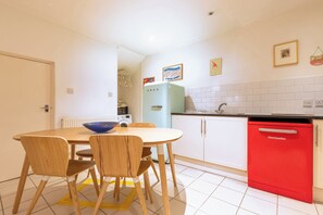 A compact kitchen with a dining table, chairs, a red dishwasher, and a vintage-style refrigerator. - One of a Kind 2BDR Flat in Shoreditch (London)