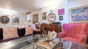 Un salon avec une table basse en verre, un canapé rouge, un canapé de couleur foncée, un meuble en bois et divers tableaux encadrés accrochés aux murs.