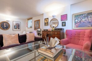 A living room with a glass coffee table, a red sofa, a dark-colored sofa, a wooden cabinet, and various framed artworks on the walls. - One of a Kind 2BDR Flat in Shoreditch (London)