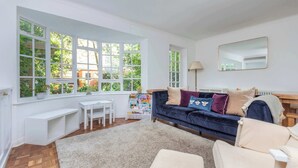 A room with a large window, a dark blue sofa, a white desk, and a white chair.