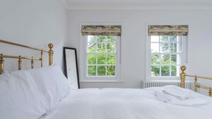 A bed with white linens, a gold-framed headboard, and two windows with curtains.
