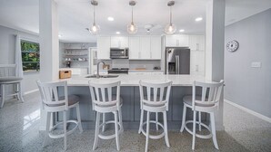 A modern kitchen with white cabinetry, a central island with bar stools, pendant lighting, and a built-in microwave. - Island Sanctuary: Canal Home with Pool, Pets OK! (Sanibel)