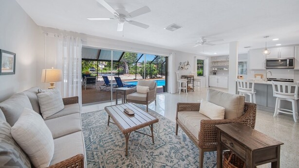 A spacious living area with a sofa, coffee table, and chairs, a dining table, and a kitchen area with white cabinets and a microwave. - Island Sanctuary: Canal Home with Pool, Pets OK! (Sanibel)