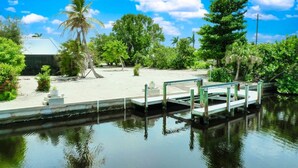 A calm waterway with a dock, surrounded by lush greenery and a clear blue sky. - Island Sanctuary: Canal Home with Pool, Pets OK! (Sanibel)