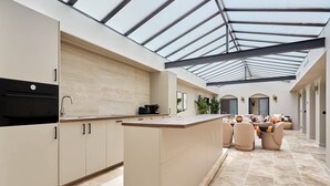 Une cuisine moderne dotée d’un grand îlot central, d’un coin repas avec des chaises et d’un plafond en verre.