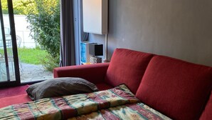 A room with a red sofa, a patterned bedspread, and a view of greenery outside. - PARISIAN FOREST  (Cesson)