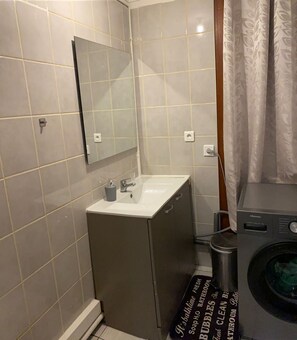 Casa de banho compacta com lavatório, espelho e máquina de lavar roupa.
