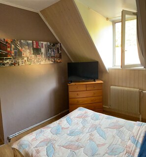Um quarto com teto inclinado, cômoda, cama com colcha estampada, radiador e parede com pôster de paisagem urbana.