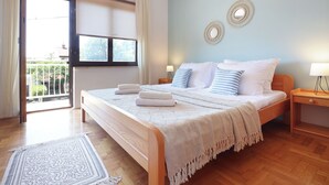 Een slaapkamer met een groot bed, een houten nachtkastje, een raam met gordijnen en uitzicht op het omliggende landschap.