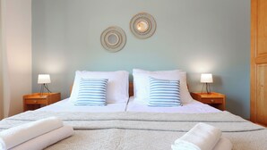 Een tweepersoonsbed met witte en blauw gestreepte kussens, twee ronde spiegels aan de muur en twee bedlampjes.