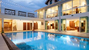 Une maison moderne à deux étages, dotée d’une piscine, de grandes baies vitrées et d’un balcon agrémenté de guirlandes lumineuses.