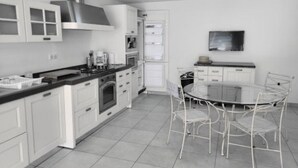 A modern kitchen with white cabinetry, a stainless steel range hood, a built-in oven, and a round dining table with four chairs.