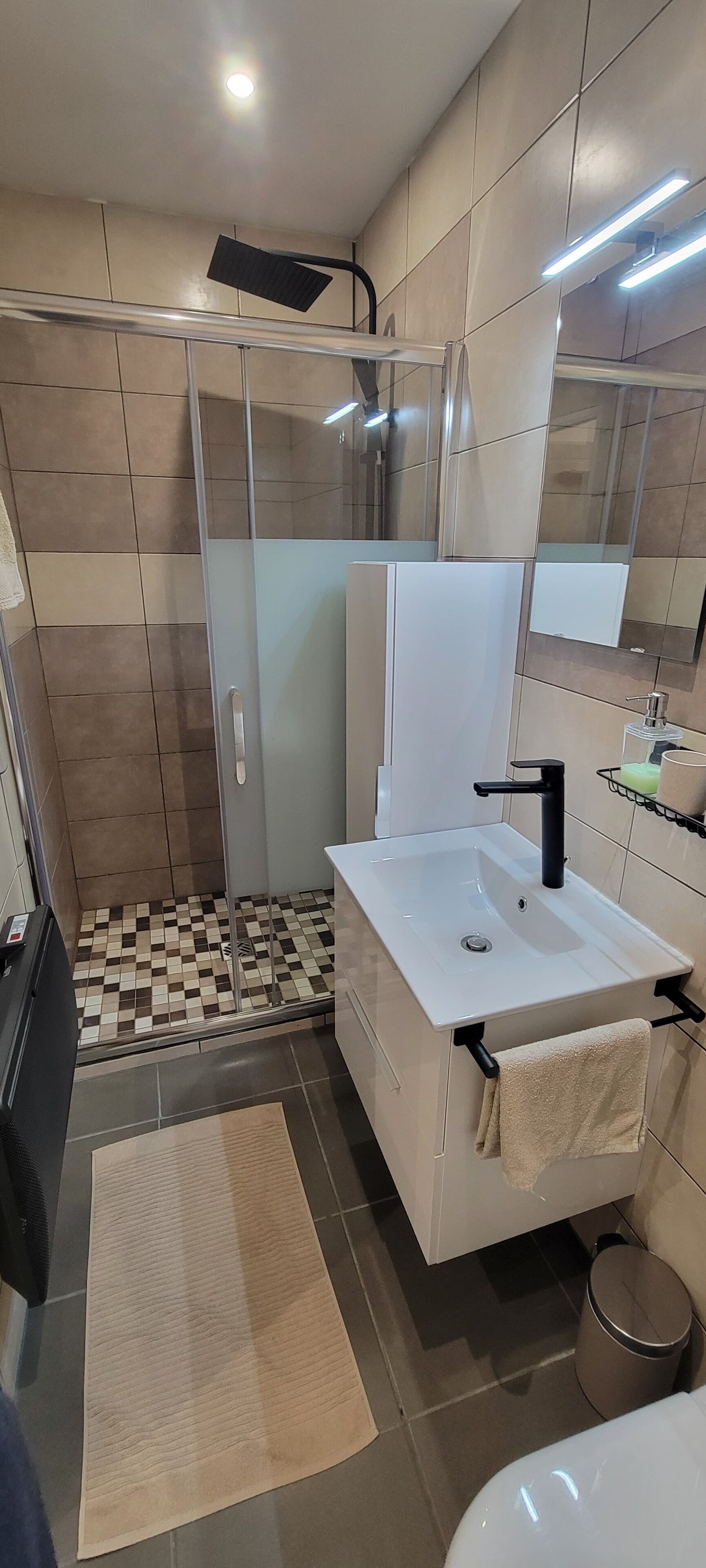 Un baño moderno con cabina de ducha de vidrio, un lavabo blanco y un espejo grande.