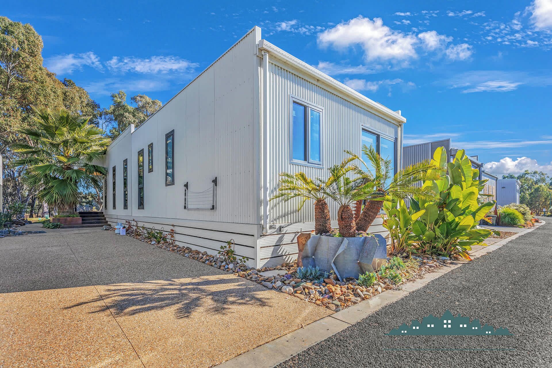 A white single-story house with a small porch, surrounded by tropical plants and a clear blue sky.