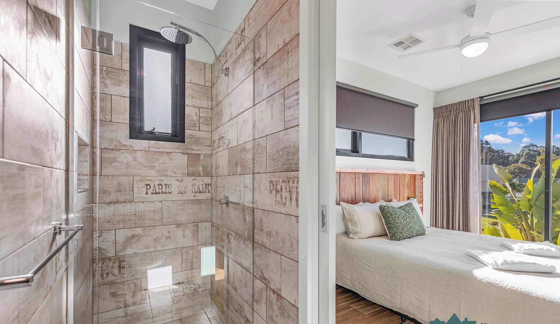 Une salle de bain moderne équipée d’une douche, d’un meuble-lavabo et d’un miroir. La salle de bain dispose d’une grande fenêtre et offre une vue sur l’extérieur.