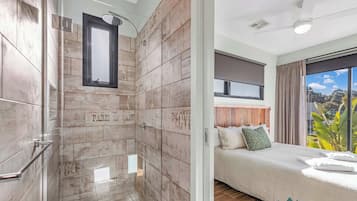 Une salle de bain moderne équipée d’une douche, d’un meuble-lavabo et d’un miroir. La salle de bain dispose d’une grande fenêtre et offre une vue sur l’extérieur.