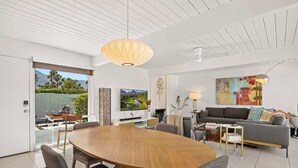 Ein modernes Wohnzimmer mit einem Holzesstisch, grauen Sofas und einem großen Fenster mit Blick auf Grünflächen und Berge.