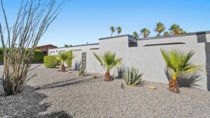 A modern building with a gravel courtyard, palm trees, and a clear blue sky. - Mid-Century Palm Springs Retreat with Pool (Palm Springs)
