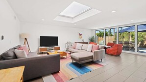 A modern living room with a sofa, armchairs, a TV, and a large window. - Mid-Century Palm Springs Retreat with Pool (Palm Springs)