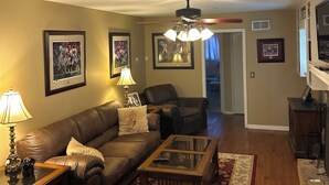 A living room with a brown leather sofa, a glass coffee table, a patterned rug, and framed pictures on the walls.