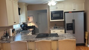 A kitchen with a central island, bar stools, a microwave, a refrigerator, and wooden flooring.