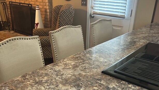 A kitchen with a granite countertop, chairs with metal studs, and a door with a window.
