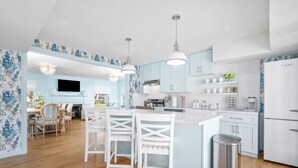 A modern kitchen with light blue cabinets, white countertops, and a central island with bar stools.