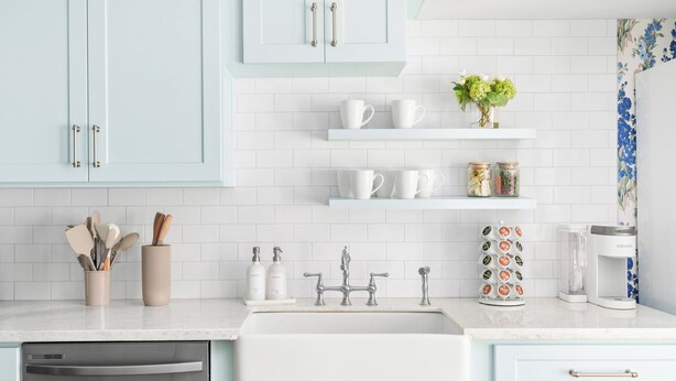 A modern kitchen with light blue cabinets, white countertops, and a stainless steel dishwasher.