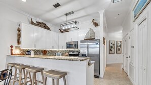 A modern kitchen with white cabinets, a granite countertop, and a stainless steel refrigerator. There are bar stools and a hanging light fixture above the island. - Lakefront 402, Upgraded 3-bd, 3-bath lakefront villa just steps to the beach! (Miramar Beach)