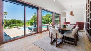 Un espace repas moderne doté de grandes fenêtres, offrant une vue sur la piscine, et comprenant une table à manger avec des chaises.