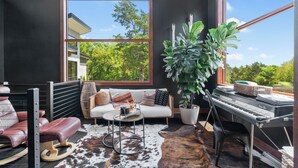Un salon moderne avec une grande fenêtre, un canapé, une table basse, un clavier et une plante en pot.