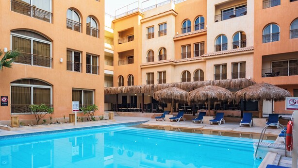 Ein Pool mit Liegestühlen und Sonnenschirmen, umgeben von mehrstöckigen Gebäuden mit Balkonen.