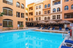 A swimming pool with lounge chairs and umbrellas, surrounded by multi-story buildings with balconies. - La Rosa Boho Aquapark Hotel (Hurghada)