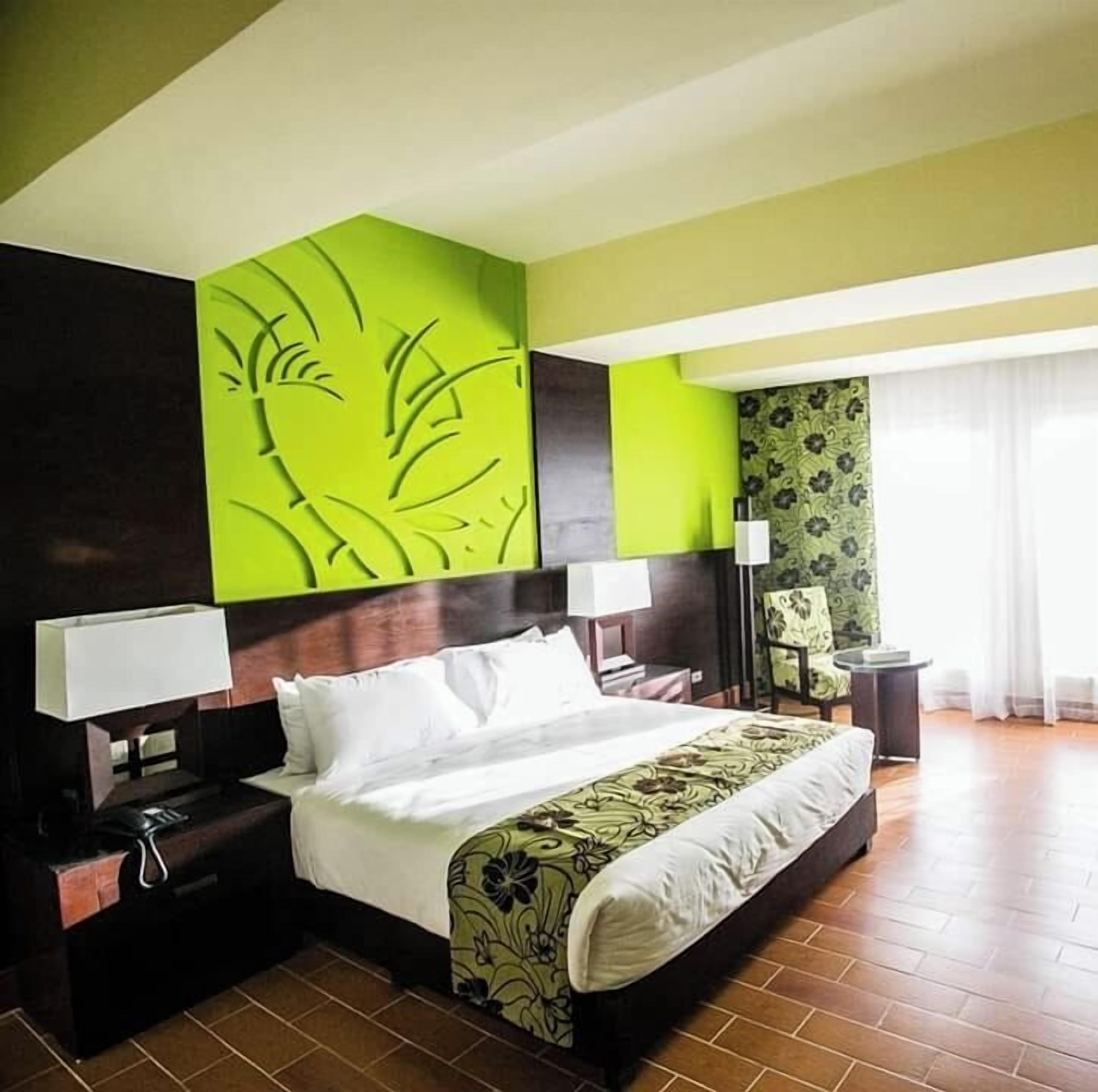 Una camera d'albergo con un letto grande, due comodini, una sedia e una finestra con tende.