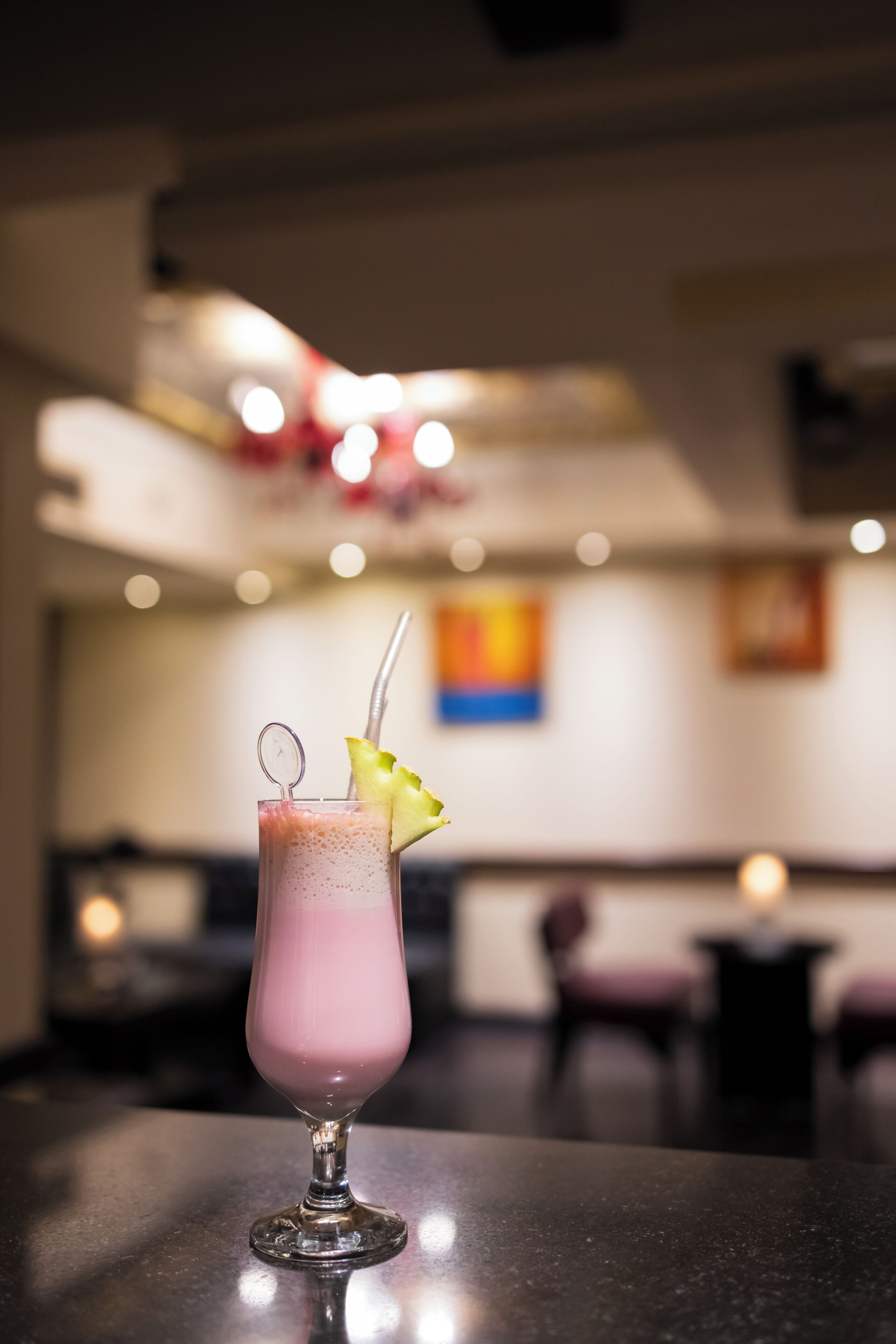 En lyserød cocktail med sugerør og et limeskive på en bardisk.