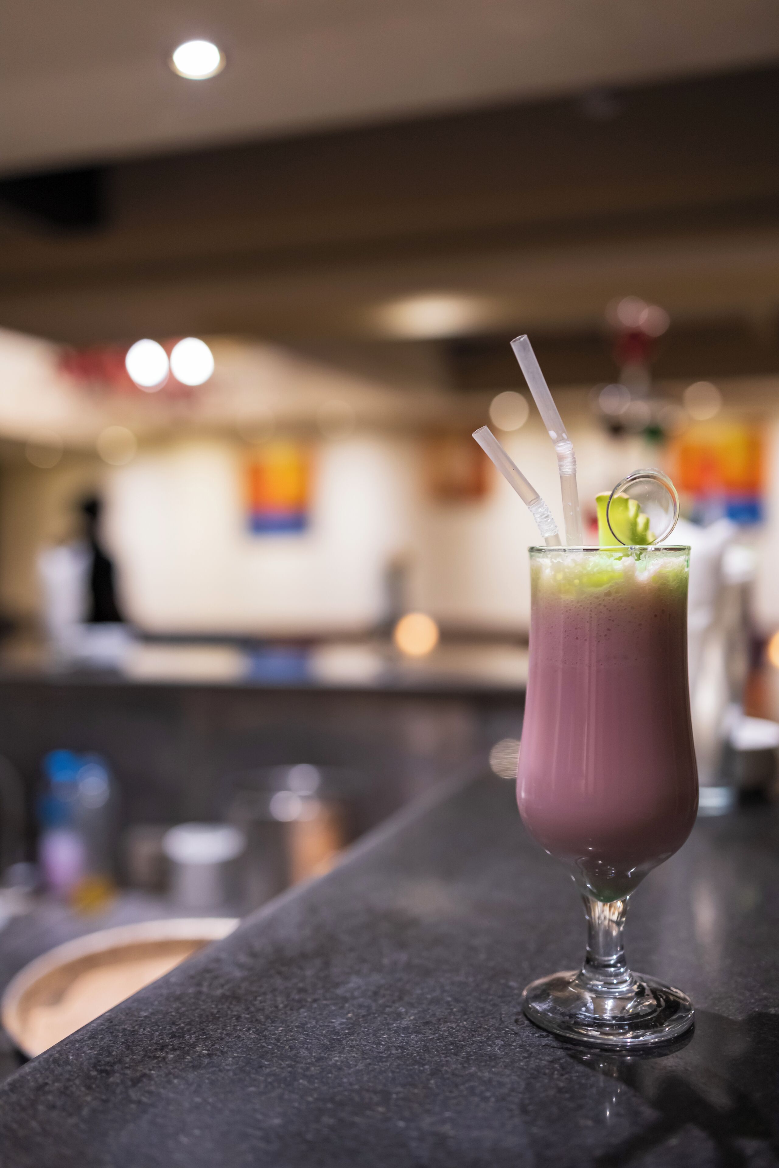 Een bar met een glas paars drankje, twee rietjes en een limoen.