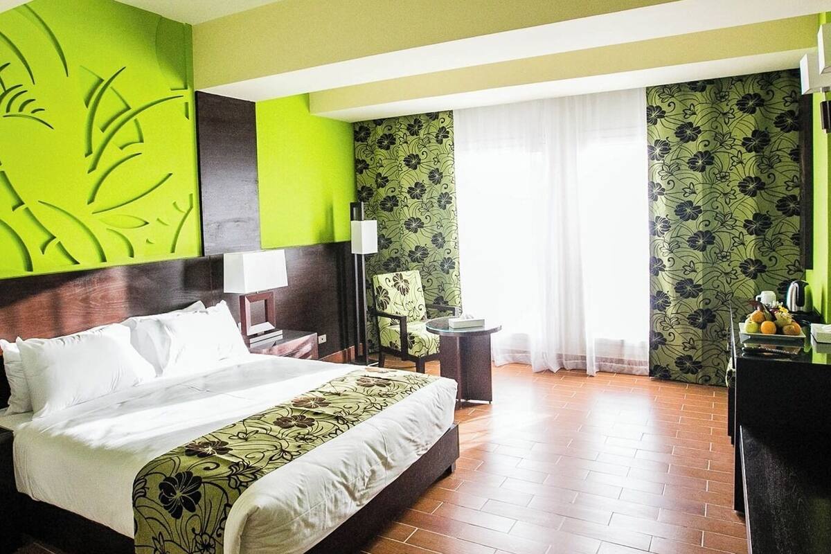 Habitación de hotel con cama, escritorio, silla y ventana con cortinas.