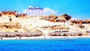 Ein Strand mit strohgedeckten Hütten und einem Schild mit der Aufschrift 'Mahmya'.