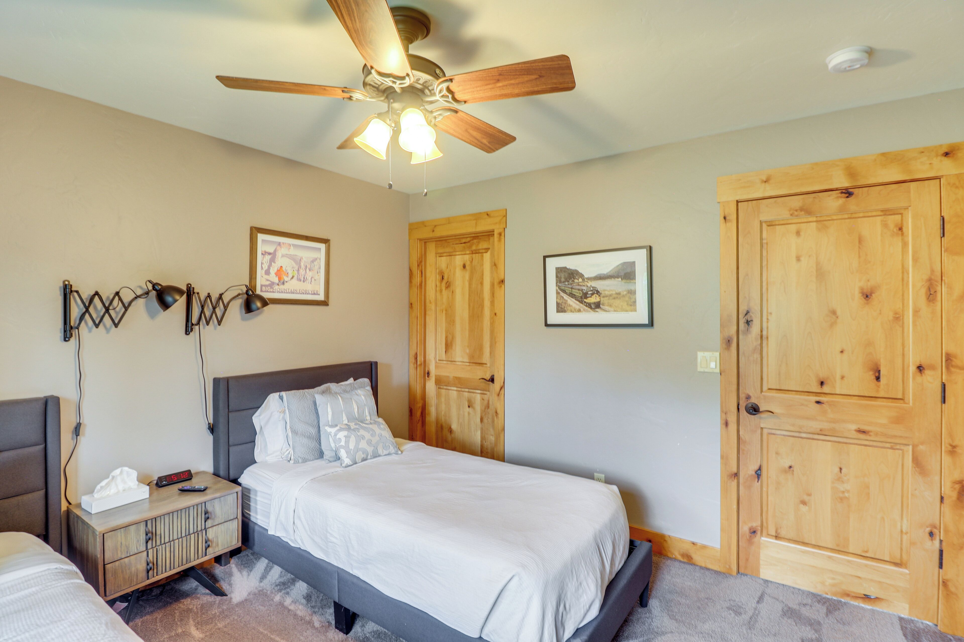 A bedroom with a bed, a nightstand, a ceiling fan, wooden doors, and framed pictures on the wall.
