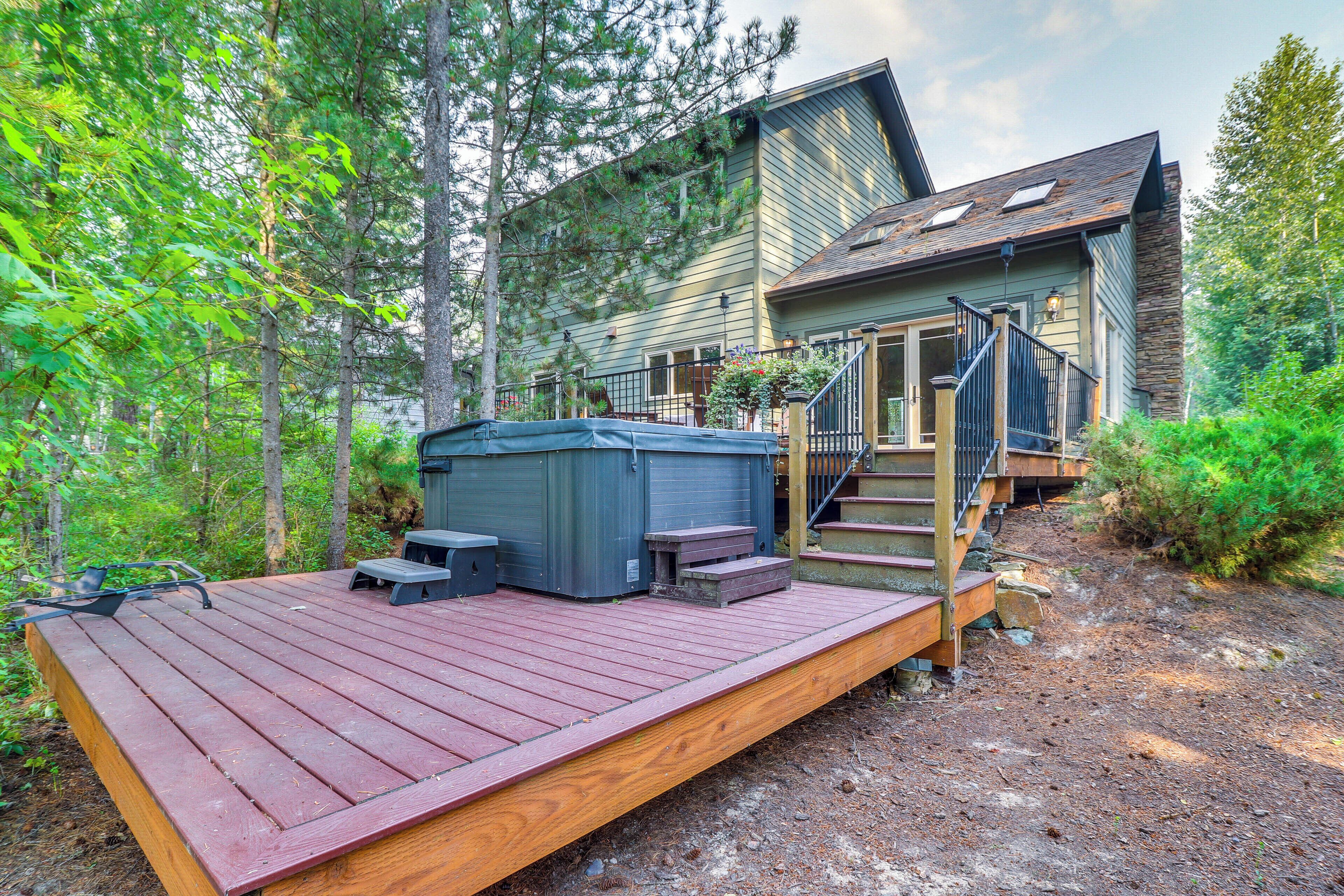 A wooden deck with a hot tub, steps leading to a house, and a forested backdrop.