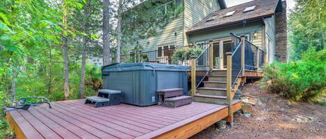 A wooden deck with a hot tub, steps leading to a house, and a forested backdrop.