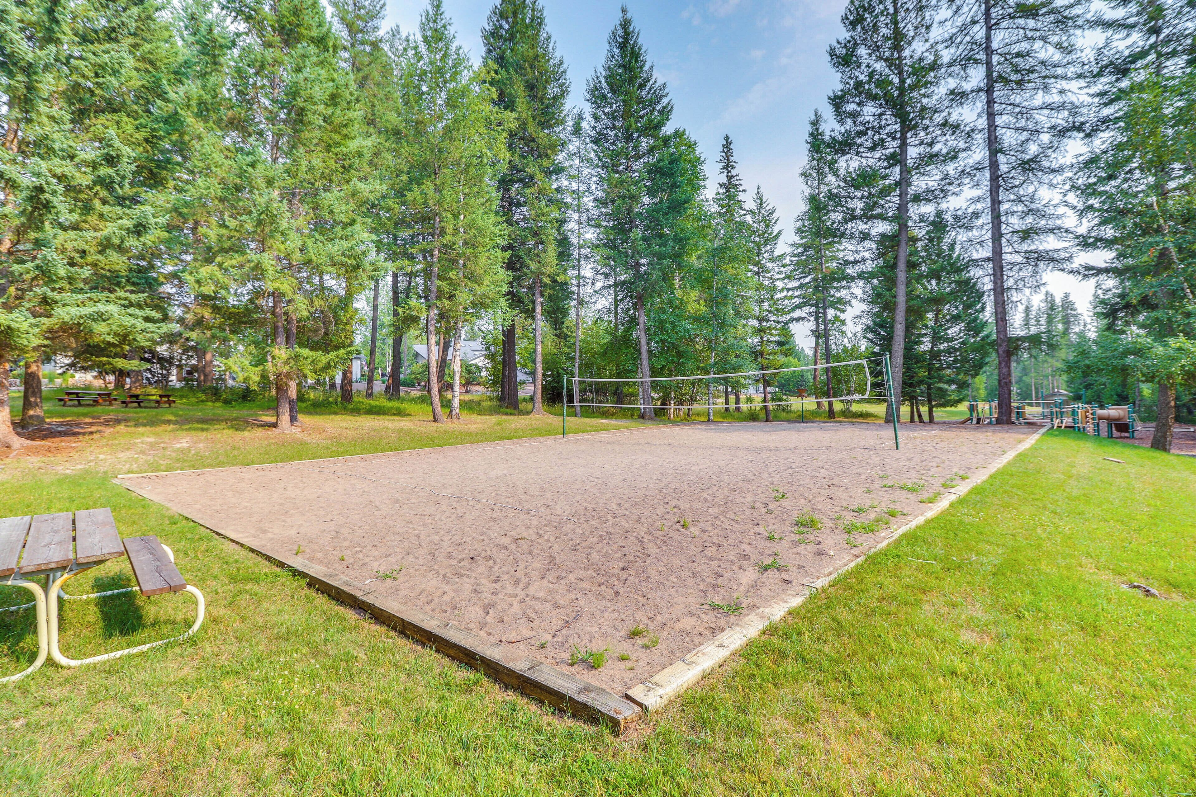 Cancha de voleibol rodeada de árboles, con mesas de picnic y un espacio cubierto de césped.