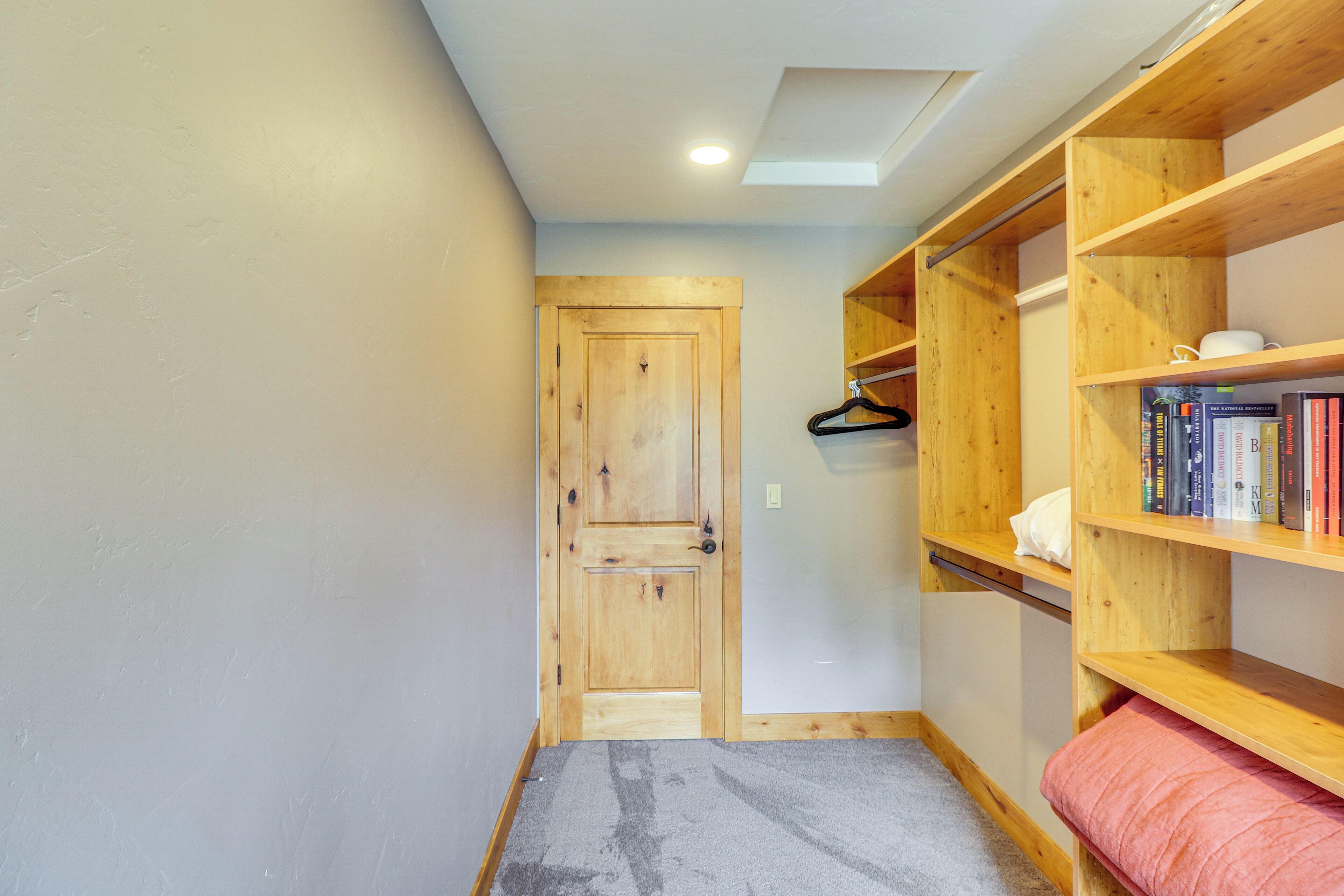 A hallway with a wooden door, a bookshelf with books, and a grey carpet.