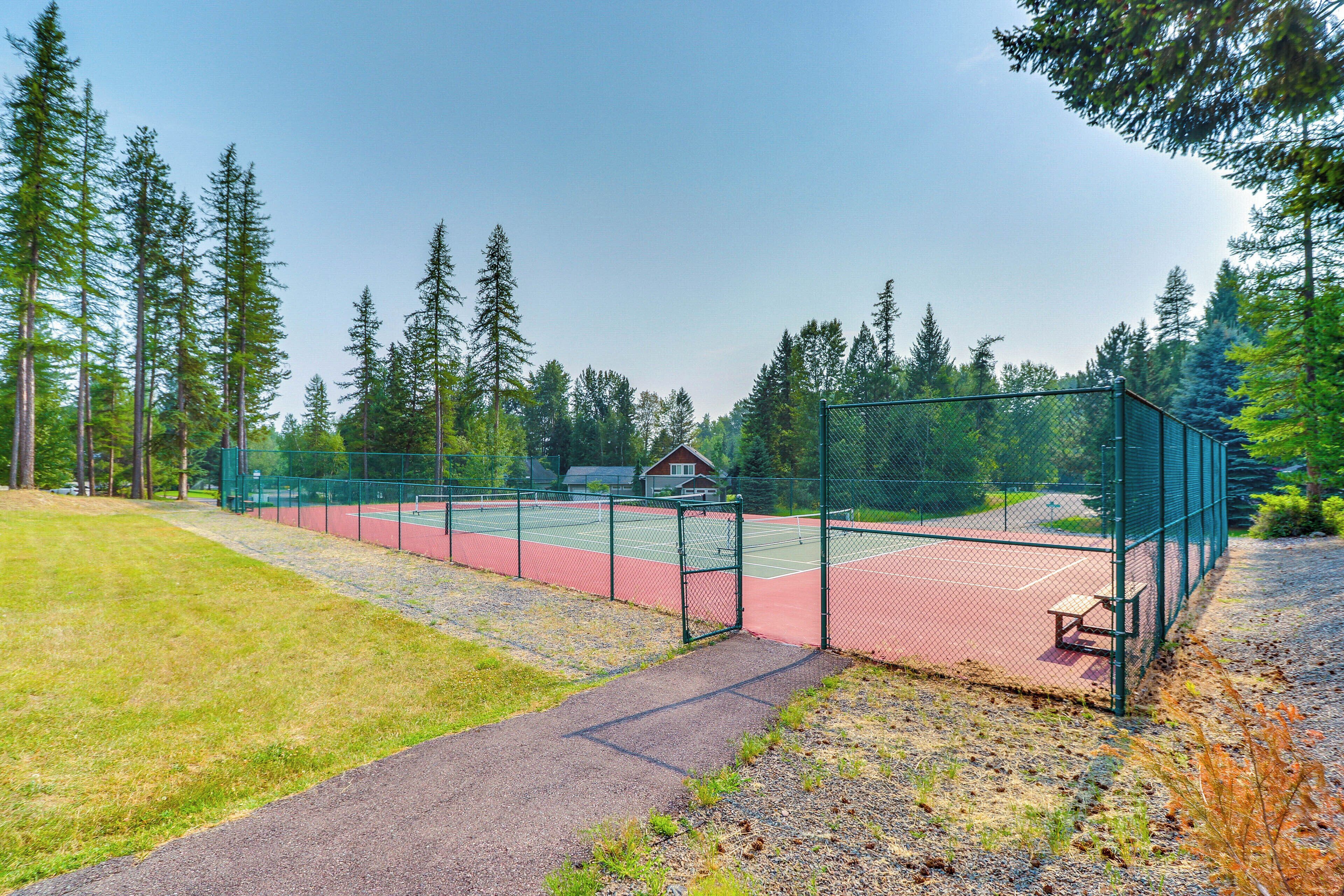 A tennis court surrounded by a green fence, with a bench and a small building in the background.
