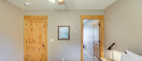 A bedroom with a wooden door, a ceiling fan, a bedside table with a lamp, and a bed.
