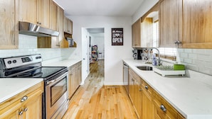 A kitchen with wooden cabinets, a stainless steel range hood, a black stove, a white countertop, and a sign that says "The Kitchen OPEN". - Hot Tub + Fire Pit: Pocono Summit Home! (Pocono Summit)