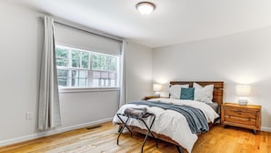 A bedroom with a wooden floor, a bed with white bedding, a nightstand with a lamp, and a window with curtains. - Hot Tub + Fire Pit: Pocono Summit Home! (Pocono Summit)