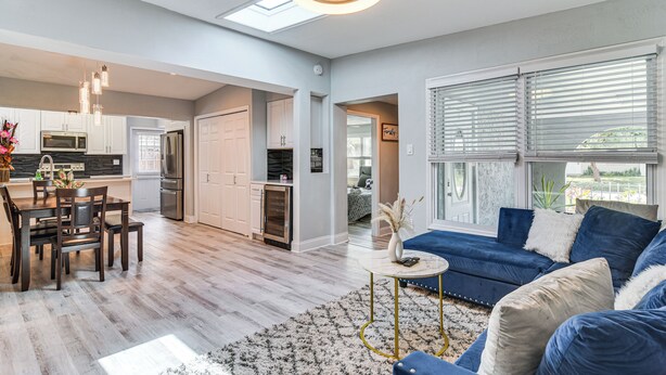 Een moderne woonkamer met een blauwe bank, een eethoek met houten stoelen, en een keuken met witte kasten.