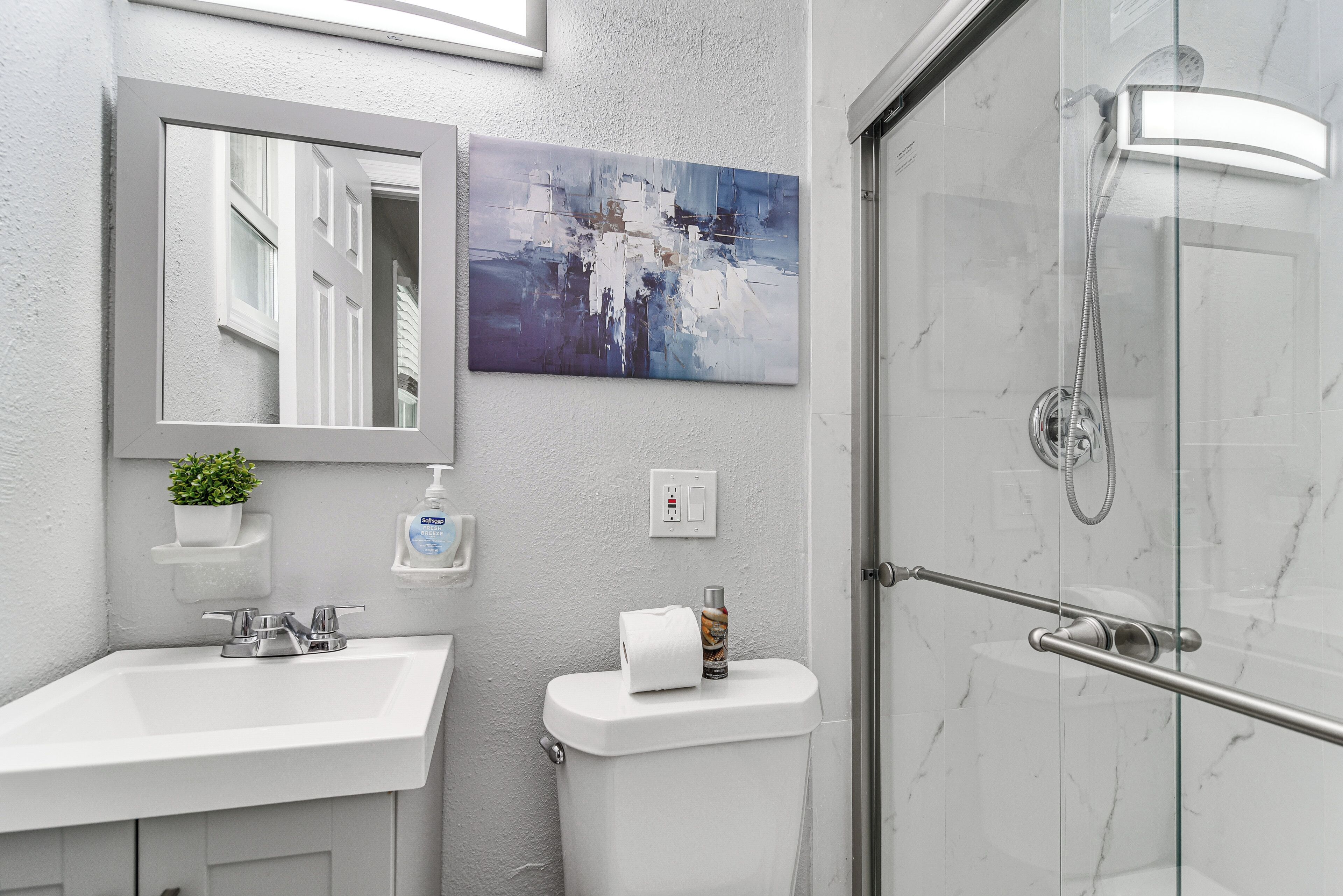 Een badkamer met een witte wastafel, een spiegel, een toilet en een douche met glazen wanden.
